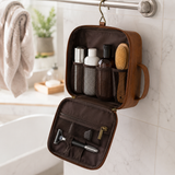 Brown leather toiletry bag hanging open by its hook in a bright bathroom, filled with toiletries