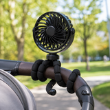 Black mini fan wrapped around a stroller handlebar outdoors