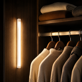 Motion-sensor LED light bar illuminating a wardrobe interior with warm light