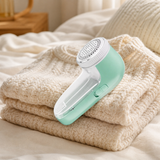 Rechargeable fabric shaver resting on a folded knit sweater in a cozy bedroom