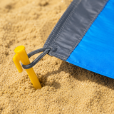 Close-up of a reinforced corner loop anchored with a yellow ground stake in beach sand
