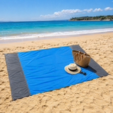 Blue beach blanket spread on golden sand with a straw sun hat and tote bag, ocean behind