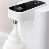 Close-up of the soap dispenser sensor panel and nozzle dispensing white foam