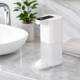 Touchless foaming soap dispenser on a marble bathroom vanity with foam on the tray